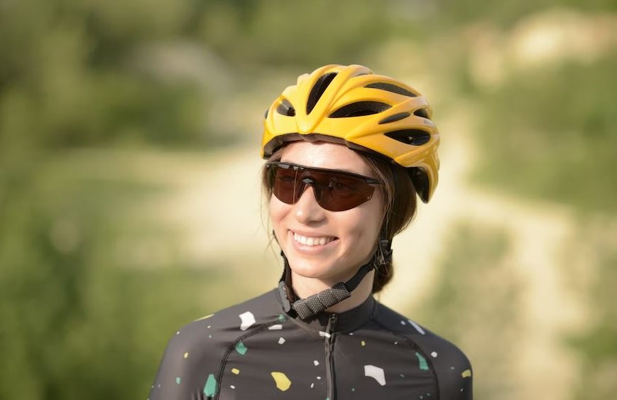 une jeune cycliste avec un casque jaune et des lunettes de velo qui sourie