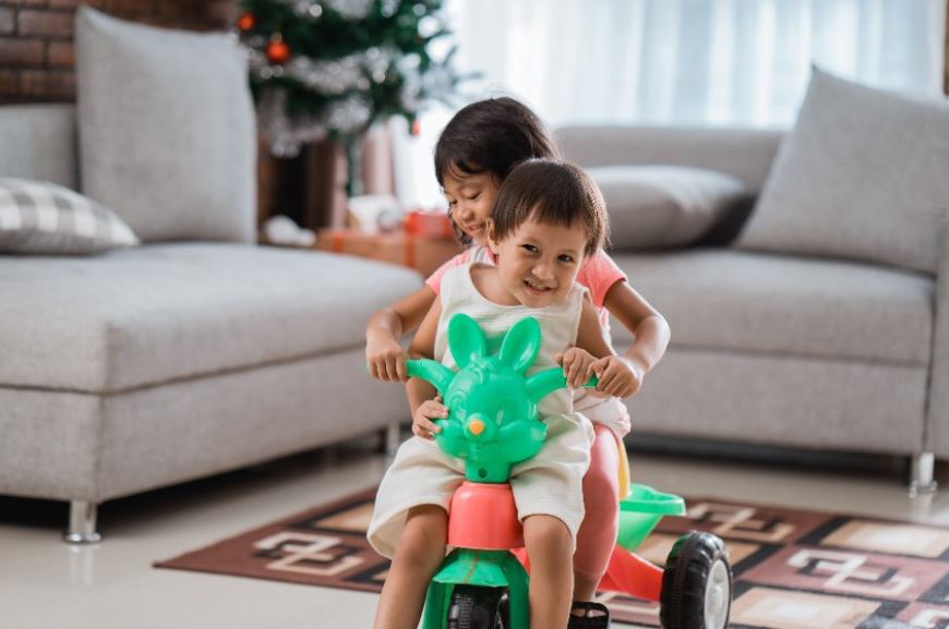 deux enfants sur un tricycle evolutif dans un salon