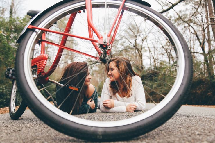 une photo tres artistique de deux femmes alongees sur le bitume avec au devant la roue et les rayons dun velo