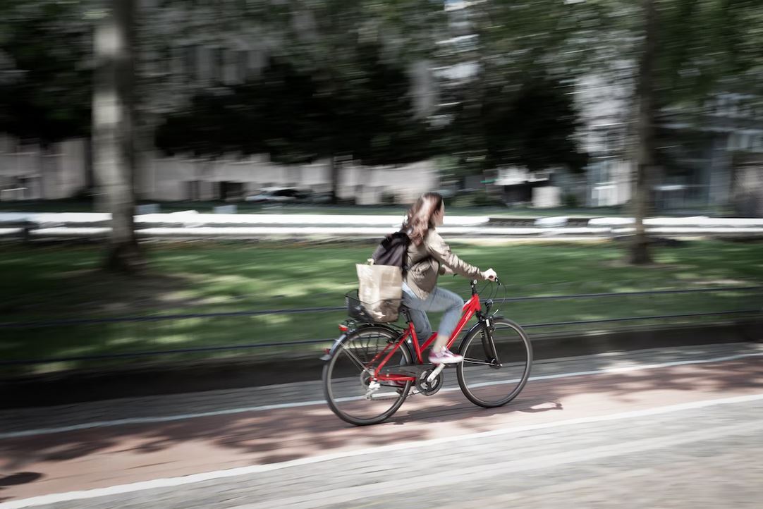 une fille sur un velo rouge qui roule en ville avec son sac de course sur le porte bagage