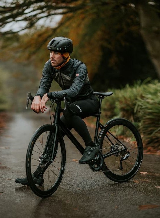 un cycliste a larret entierement habille en noir avec son velo de route de la meme couleur