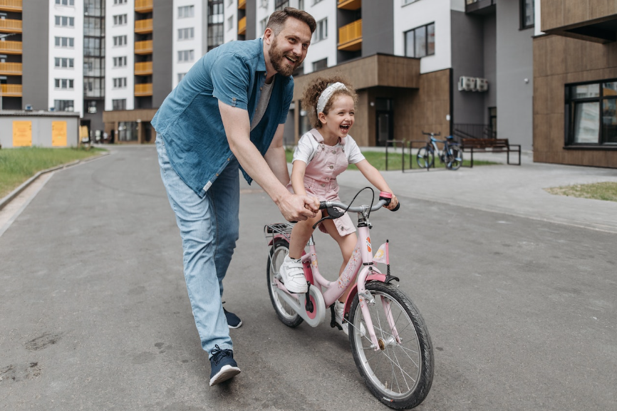 photo dun papa souriant qui apprend a faire du velo sans les roues a sa fille